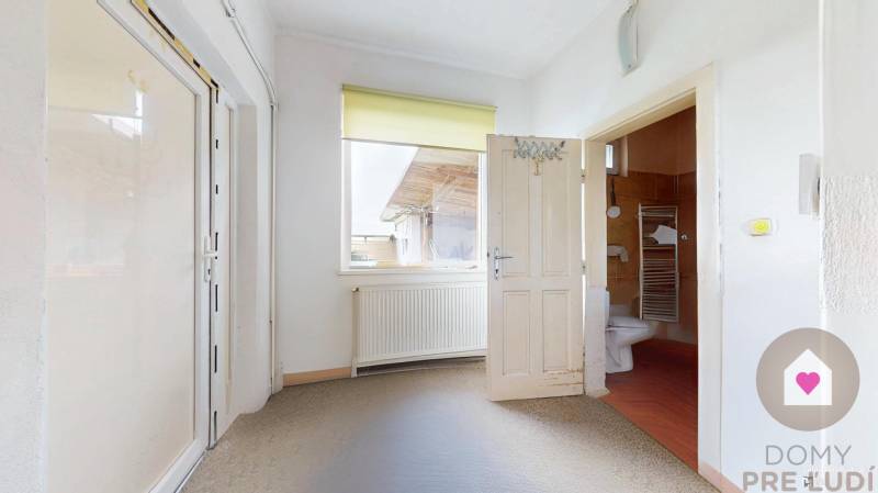 Veľký priestranný pozemok o rozlohe 7445 m2 s RD, Jelka  - Interiér rodinného domu s dverami vedúcimi do kúpeľne a radiátorom pod oknom.