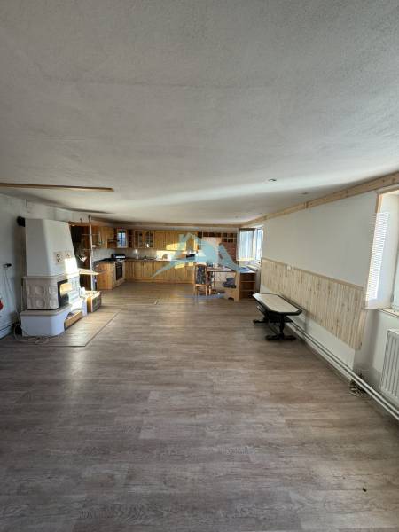 Skrytý raj v srdci prírody - Interiér rodinného domu s kuchynským kútom, murovanou pecou a podlahou s dreveným dekorom.