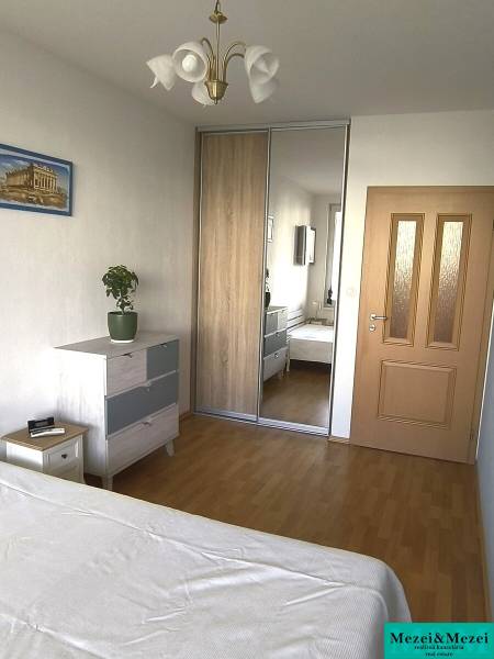 Na dlhodobý prenájom 2-izbový byt - kompletne zariadený, klimatizovaný - Spálňa v 2-izbovom byte s podlahou s dreveným dekorom, vstavanou skriňou a komodou.