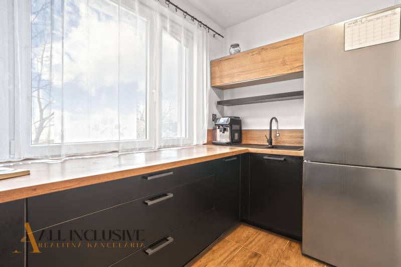 NA PREDAJ 3-IZBOVÝ BYT S PIVNICOU, SENEC - Kuchyňa v 3-izbovom byte s veľkým oknom, čiernymi skrinkami a podlahou s dreveným dekorom.