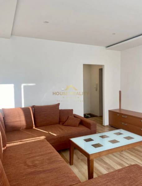 Pekný 3 izbový byt s lodžiou, ulica Nad Lúčkami, BA IV. Karlova Ves - Obývacia izba s hnedou sedačkou a stolíkom, 3-izbový byt s podlahou s dreveným dekorom.