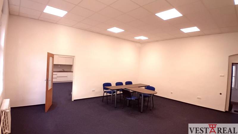 Na prenájom priestor- kancelária 60 m2 Trnava - Františkánska - Kancelária s modrými stoličkami a stolmi, biela stena, otvorené dvere k malej kuchynke.