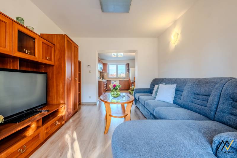 2 IZBOVÝ BYT PREŠOV, ULICA TARASA ŠEVČENKA - Obývacia izba v 2-izbovom byte s podlahou s dreveným dekorom a presvetlenou kuchyňou.