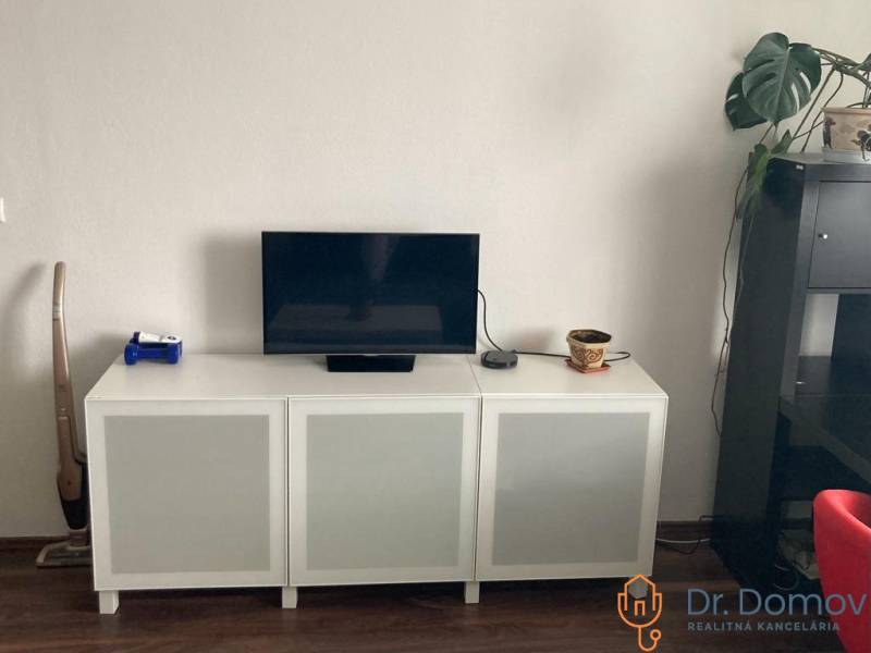 NA PRENÁJOM ÚTULNÝ 1-IZBOVÝ BYT, ČIASTOČNÁ REK., KAROLA ADLERA, BA - Televízor a biela skrinka v 1-izbovom byte s podlahou s dreveným dekorom.