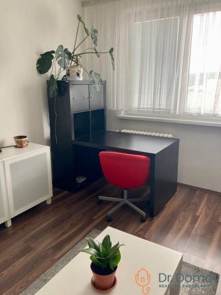 NA PRENÁJOM ÚTULNÝ 1-IZBOVÝ BYT, ČIASTOČNÁ REK., KAROLA ADLERA, BA - Pracovný kút v 1-izbovom byte s čiernym stolom, červenou stoličkou a podlahou s dreveným dekorom.