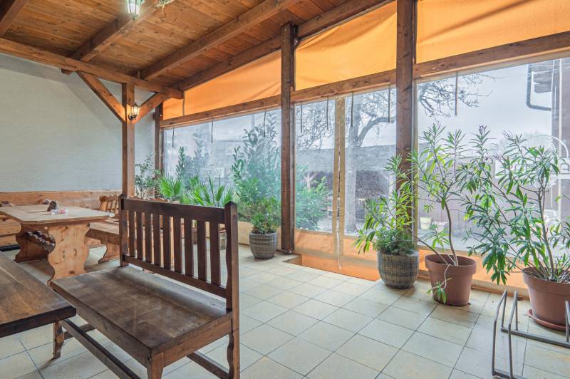 Predaj Exkluzívna ponuka elegantného penziónu s hostincom - Slnečný priestor s dreveným sedením v Hoteloch a penziónoch, obklopený rastlinami.