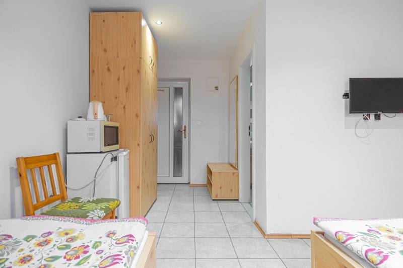 Predaj Exkluzívna ponuka elegantného penziónu s hostincom - Interiér penziónu s posteľami, televízorom, skriňou, mikrovlnkou a chladničkou.