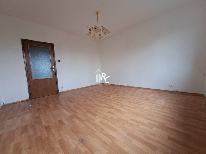 REZERVOVANÉ 2-izbový byt s nádherným výhľadom v pôvodnom stave   - Izba v 2-izbovom byte s bielymi stenami a podlahou s dreveným dekorom.