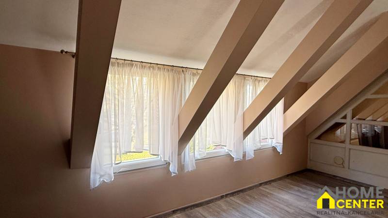 Na predaj unikátna dvojpodlažná budova na podnikanie aj bývanie - Interiér podkrovia s oknami a podlahou s dreveným dekorom.