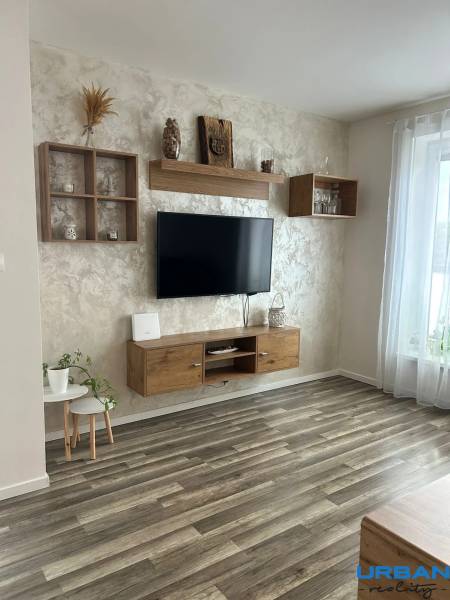Praktický 3-izbový byt v súkromnej ulici v Šamoríne - Obývačka v 3-izbovom byte s podlahou s dreveným dekorom, zavesenou TV a dekoráciami.