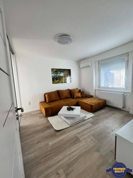 PREDAJ: 2 izbový tehlový byt-komplet.rek. - KOMÁRNO - Svetlá obývacia izba v 2-izbovom byte s hnedou sedačkou a stolíkom na podlahe s dreveným dekorom.