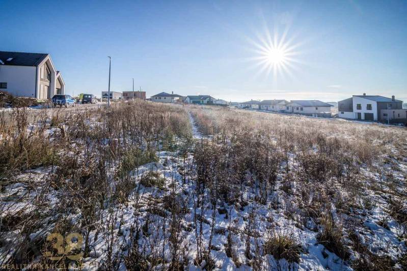 Stavebný pozemok v lokalite Medzi Vodami - Zasnežený pozemok v Mlynici s obydliami na pozadí, ideálny pre bývanie.