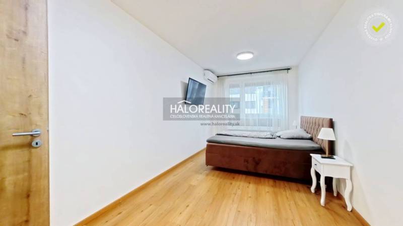 Predaj, dvojizbový byt Bratislava Ružinov, Trnavská ... - Spálňa v 2-izbovom byte s posteľou, nočným stolíkom a televízorom, má podlahu s dreveným dekorom.