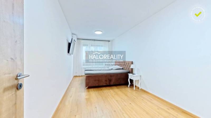 Predaj, dvojizbový byt Bratislava Ružinov, Trnavská ... - Svetlá spálňa s posteľou, nočným stolíkom a TV v 2-izbovom byte, podlaha s dreveným dekorom.