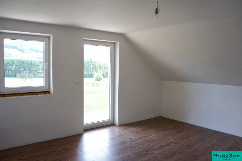 Na predaj – veľkorysý rodinný dom s úžasným výhľadom a pozemkom - Svetlá izba s oknami, podlaha s dreveným dekorom a presklenými dverami v rodinnom dome.