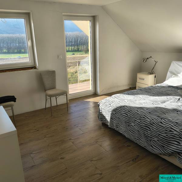 Na predaj – veľkorysý rodinný dom s úžasným výhľadom a pozemkom - Svetlá spálňa v rodinnom dome s posteľou, stoličkou a podlahou s dreveným dekorom.