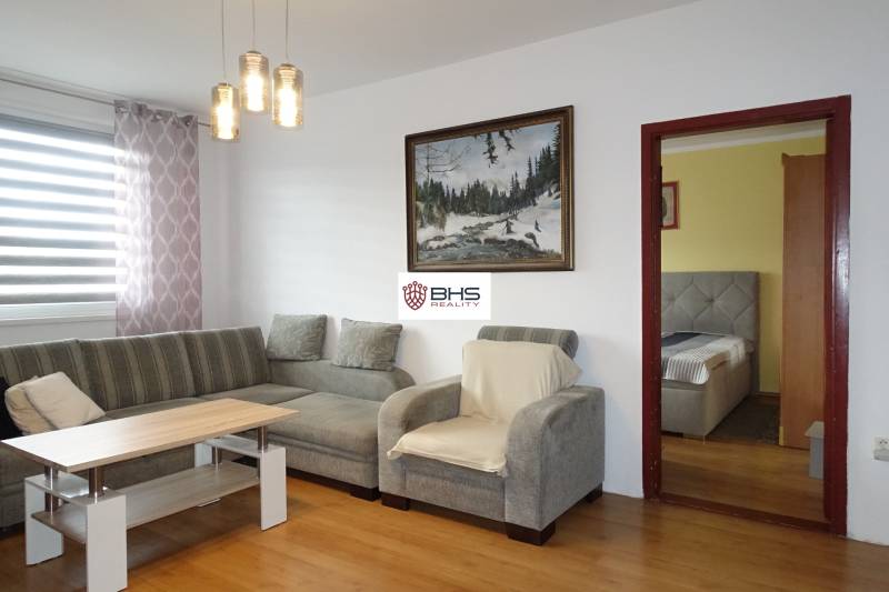 PREDAJ- 3-iz. byt, Homolova - Dúbravka, 67 m2, 11./12. posch., lodžia - Obývacia izba v 3-izbovom byte s pohovkou, kreslom a podlahou s dreveným dekorom.