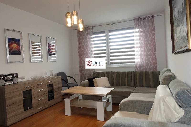 PREDAJ- 3-iz. byt, Homolova - Dúbravka, 67 m2, 11./12. posch., lodžia - Svetlá obývačka s rohovou sedačkou, stolíkom a komodou v 3-izbovom byte.