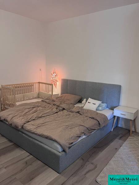 Na predaj moderný 4-izbový byt s veľkou terasou a súkromnou záhradou - Spálňa s čalúnenou posteľou, detskou postieľkou a nočným stolíkom v 4-izbovom byte.