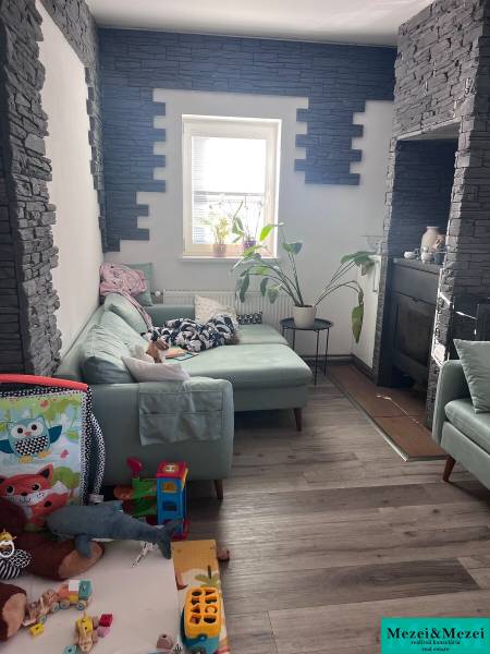 Na predaj moderný 4-izbový byt s veľkou terasou a súkromnou záhradou - Obývačka so zelenou sedačkou, hračkami, rastlinami a stenami s kamenným obkladom v 4-izbovom byte.