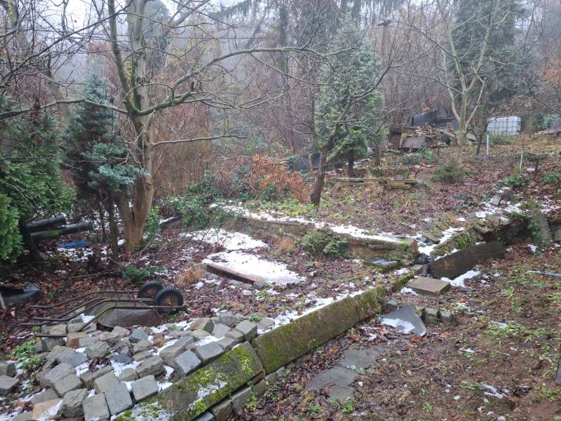 Predaj rodinného domu s pozemkom v  lukratívnej časti mesta Bratislava - Záhrada pri rodinnom dome na Búdkovej v Bratislave - Staré Mesto, s rozbitým plotom a stromami.