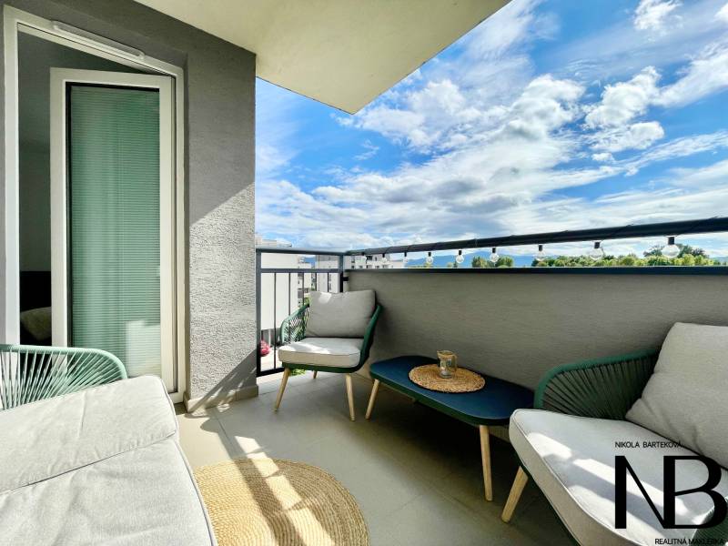 Na predaj štýlový 2-izbový byt s loggiou a parkovaním – TN, Na Pažiti - Balkón 2-izbového bytu s ratanovým nábytkom a výhľadom na mesto Trenčín na ulici Na pažiti.