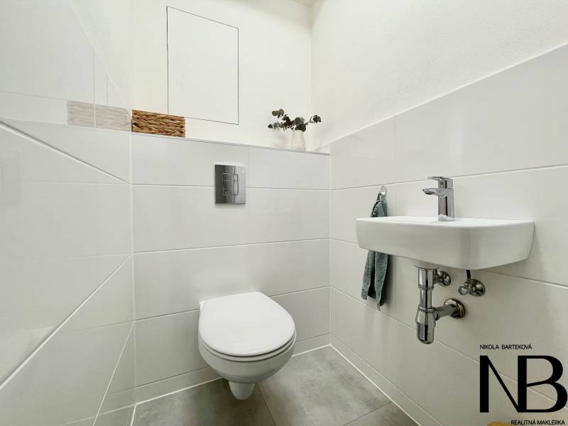 Na predaj štýlový 2-izbový byt s loggiou a parkovaním – TN, Na Pažiti - Toaleta s umývadlom v 2-izbovom byte, biele dlaždice, dekorácia na skrinke.