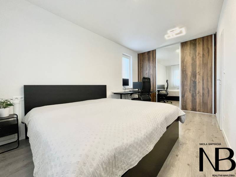 Na predaj štýlový 2-izbový byt s loggiou a parkovaním – TN, Na Pažiti - Dvojposteľ v 2-izbovom byte, šatník so zrkadlom a pracovný kút na drevenom dekore.