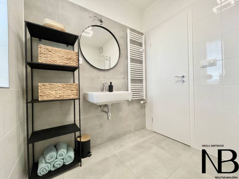 Na predaj štýlový 2-izbový byt s loggiou a parkovaním – TN, Na Pažiti - Kúpeľňa v 2-izbovom byte s umývadlom, regálom a uterákmi na dlažbe.