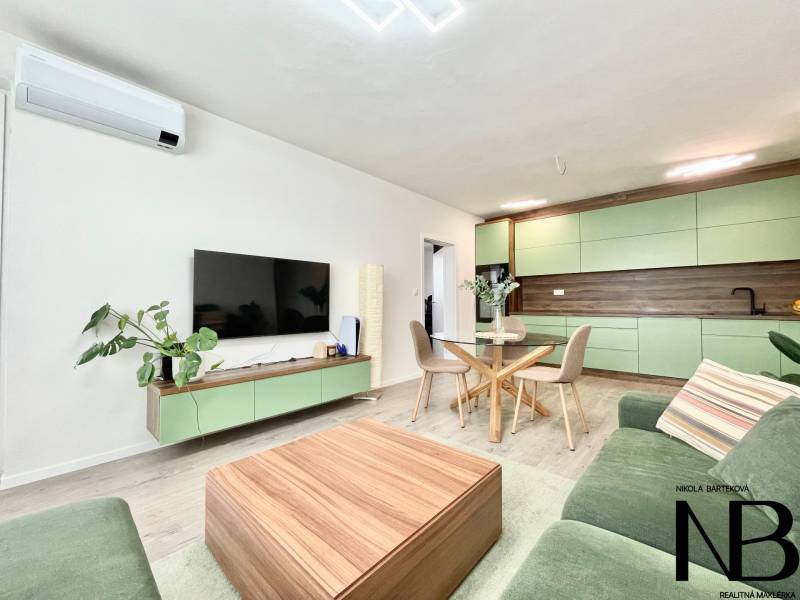 Na predaj štýlový 2-izbový byt s loggiou a parkovaním – TN, Na Pažiti - Obývacia izba v 2-izbovom byte s kuchyňou a podlahou s dreveným dekorom.