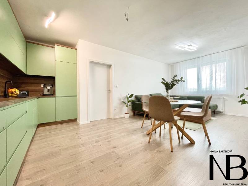 Na predaj štýlový 2-izbový byt s loggiou a parkovaním – TN, Na Pažiti - Obývačka v 2-izbovom byte s podlahou s dreveným dekorom a zelenou kuchyňou.