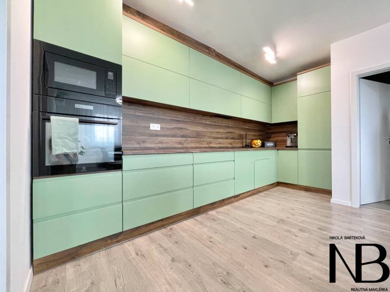 Na predaj štýlový 2-izbový byt s loggiou a parkovaním – TN, Na Pažiti - Kuchyňa v 2-izbovom byte s mätovo zelenými skrinkami a podlahou s dreveným dekorom.