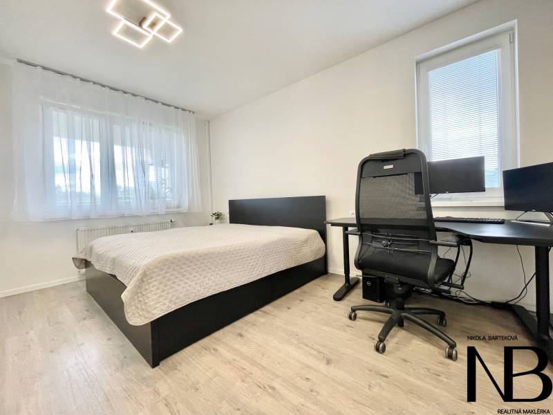 Na predaj štýlový 2-izbový byt s loggiou a parkovaním – TN, Na Pažiti - Svetlá spálňa s podlahou s dreveným dekorom v 2-izbovom byte, pracovný kút a posteľ.