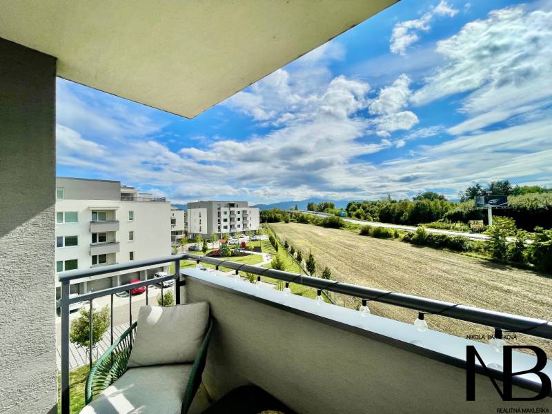 Na predaj štýlový 2-izbový byt s loggiou a parkovaním – TN, Na Pažiti - Výhľad z balkóna 2-izbového bytu na ulici Na pažiti v Trenčíne, na polia a budovy.