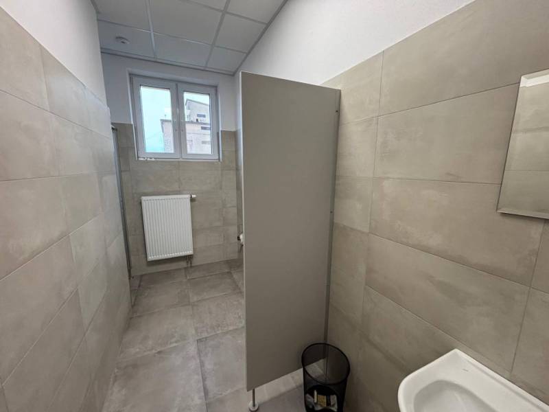 Prenájom nových kancelárskych priestorov a skladov na Teplickej ulici  - Kancelárie so sivým obkladom a záchodom, s malým oknom a rebrovým radiátorom.