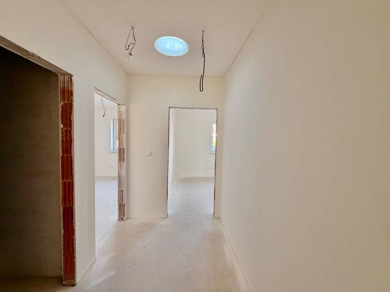 NOVOSTAVBA  ATRAKTÍVNY 4 I RODINNÝ DOM,650m2 pozemok - Chodba v rodinnom dome s dočasným osvetlením a betónovou podlahou.