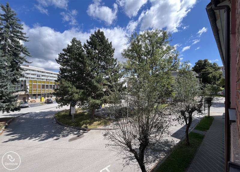 Exkluzívne | Na predaj 5i byt s garážou a záhradou v centre Ružomberka - Pohľad z 5 a viac izbového bytu na ulicu Medveckého v Ružomberku, obklopený stromami.