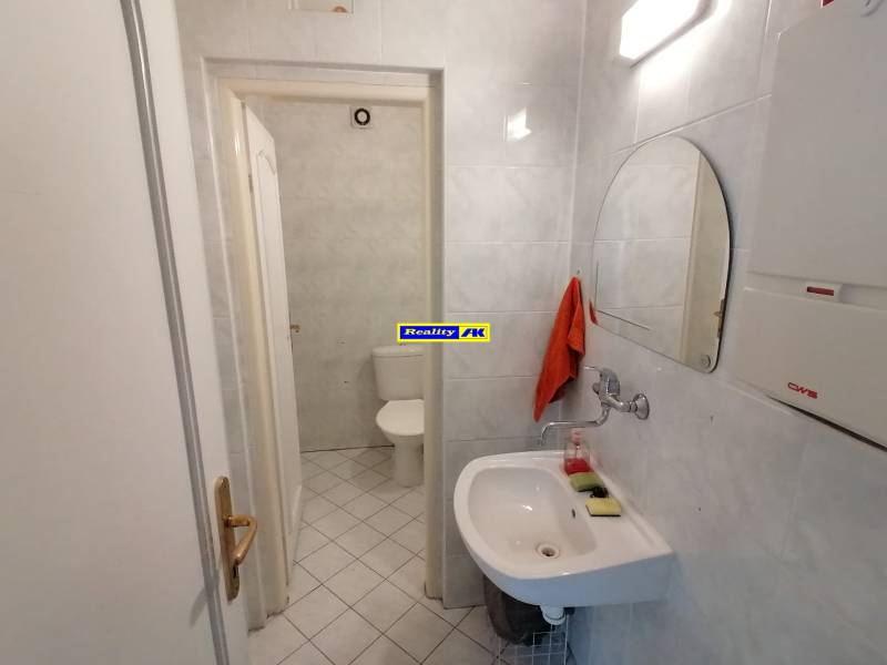 Kancelária na prenájom Martin blízke centrum, plocha 10 m2 - Kúpeľňa v kanceláriách so zrkadlom, umývadlom a toaletou na bielych obkladoch.