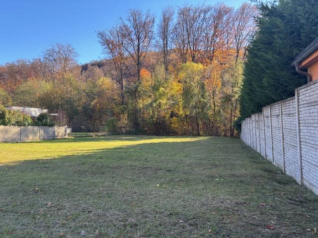 Na predaj veľký stavebný pozemok v atraktívnej štvrti Marianky - Pozemky - bývanie na Karpatskej ulici, Marianka s trávnatou plochou a stromami na pozadí.