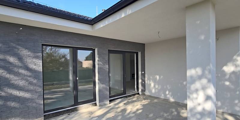 4 izbový BUNGALOV novostavba (VYSTAVBA) Piešťany, kvalitné prevedenie - Terasa rodinného domu v Piešťanoch s veľkými presklenými dverami a sivými stenami.