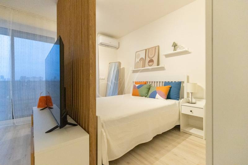 Slnečný 1,5i byt s loggiou a parkovaním - 1-izbový byt s posteľou, televízorom a dekoratívnymi vankúšmi. Podlaha s dreveným dekorom.