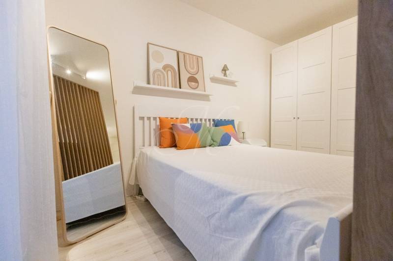 Slnečný 1,5i byt s loggiou a parkovaním - Spálňa v 1-izbovom byte s posteľou, farebnými vankúšmi, zrkadlom a veľkou skriňou.