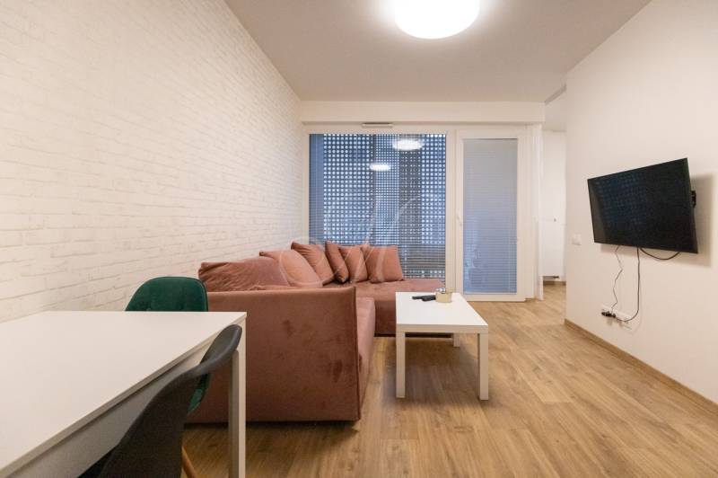 Zariadený 2i byt s lodžiou v rezidencii Pri Mýte - Obývacia izba v 2-izbovom byte s pohovkou, televízorom a podlahou s dreveným dekorom.