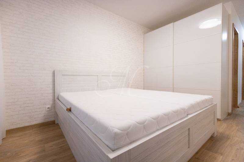 Zariadený 2i byt s lodžiou v rezidencii Pri Mýte - Svetlá spálňa s bielou posteľou, vstavaná skriňa, podlaha s dreveným dekorom v 2-izbovom byte.