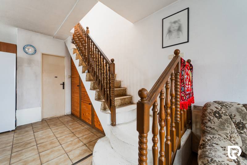 Pozemky s dvoma domami na prestavbu alebo novostavbu - Interiér rodinného domu so schodiskom, sýtočerveným kobercom a obrazom na stene.