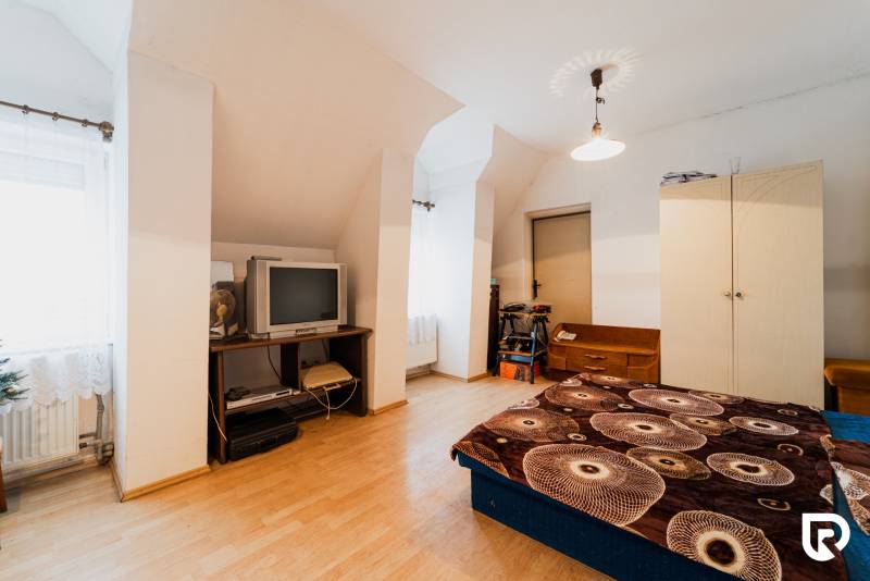 Pozemky s dvoma domami na prestavbu alebo novostavbu - Spálňa v rodinnom dome s podlahou s dreveným dekorom, starším televízorom a úložným priestorom.