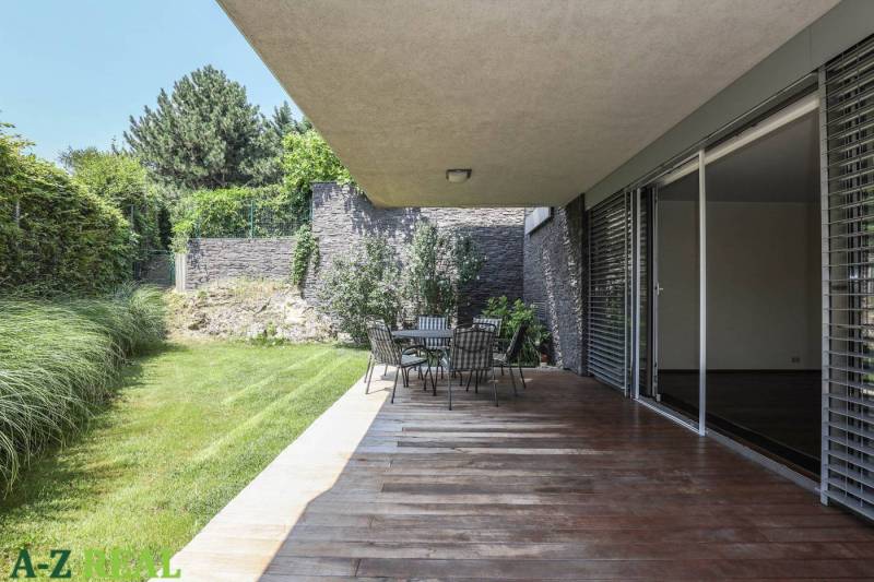 Prenájom exluzívneho 3 izbového apartmánu v Diplomat Parku. - Terasa s podlahou s dreveným dekorom, záhradným sedením a zeleňou pri 3-izbovom byte.