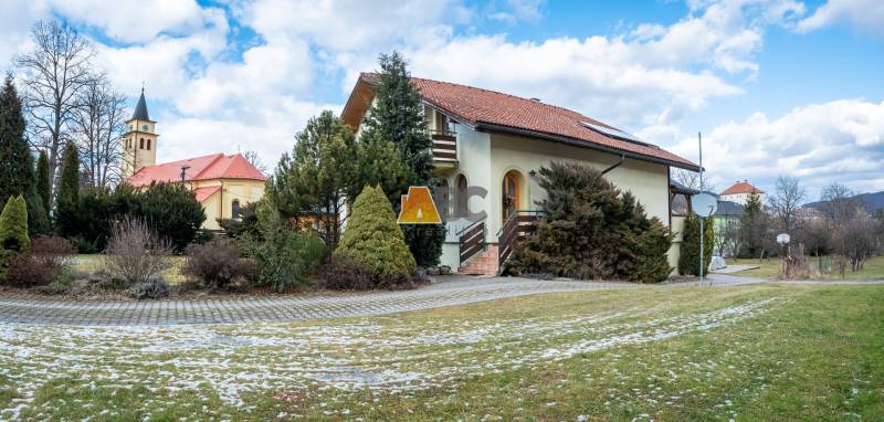 Obrovská vila pre luxusný život aj podnikanie (pripravujeme) - Vila na ulici Andreja Sládkoviča v Žarnovici, obklopená zeleňou, s kostolom v pozadí.