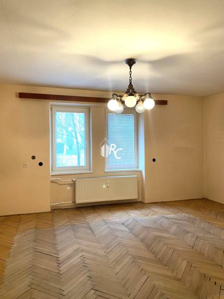 REZERVOVANÉ - Veľký 2-izbový byt s loggiou v centre Martina - Izba v 2-izbovom byte s podlahou s dreveným dekorom a visiacim lustrom.