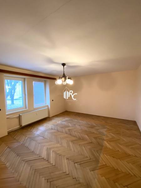 REZERVOVANÉ - Veľký 2-izbový byt s loggiou v centre Martina - Izba v 2-izbovom byte s podlahou s dreveným dekorom a centrálnym lustrom.